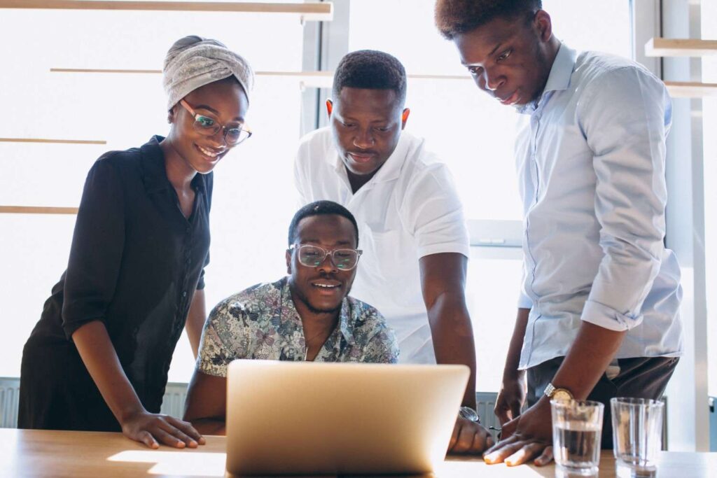 Nigerian youth gathered around a laptop to discover their purpose through collaboration.
