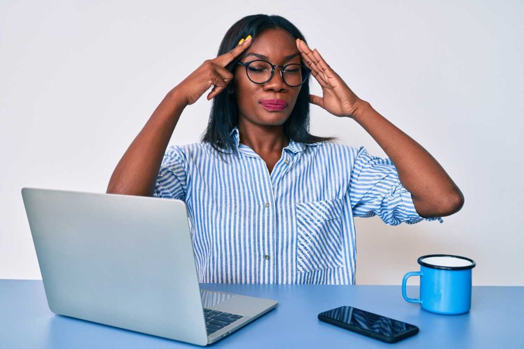 African youth entrepreneur sitting at a desk with head in hands, surrounded by papers and a dim lamp, showing signs of burnout.
