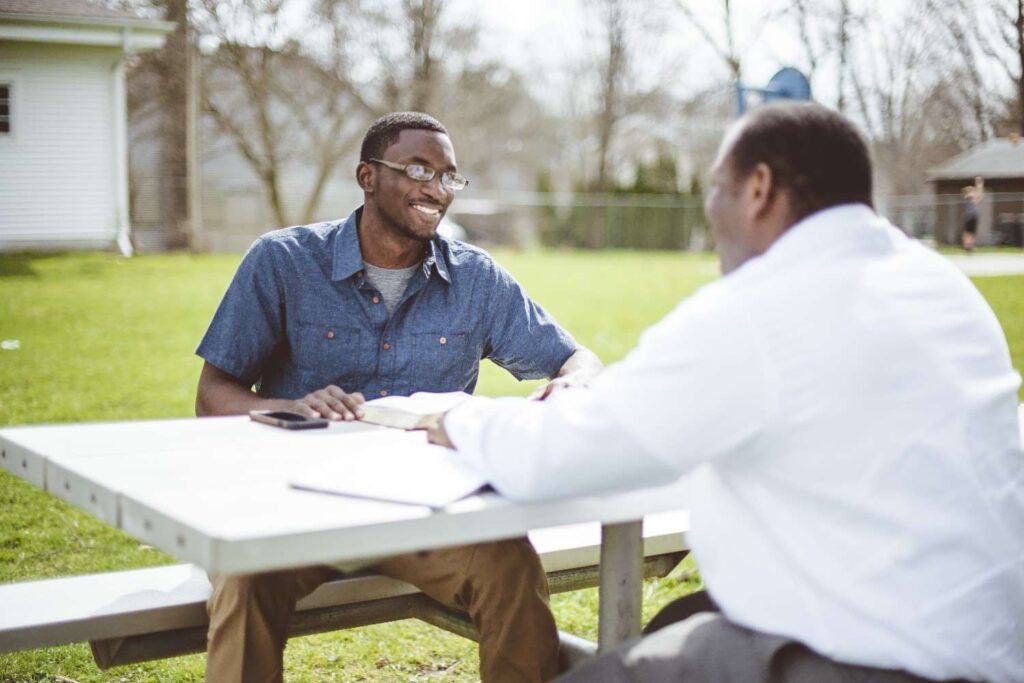 Young change-maker conducting a community listening session with an elderly resident, taking notes while demonstrating active listening