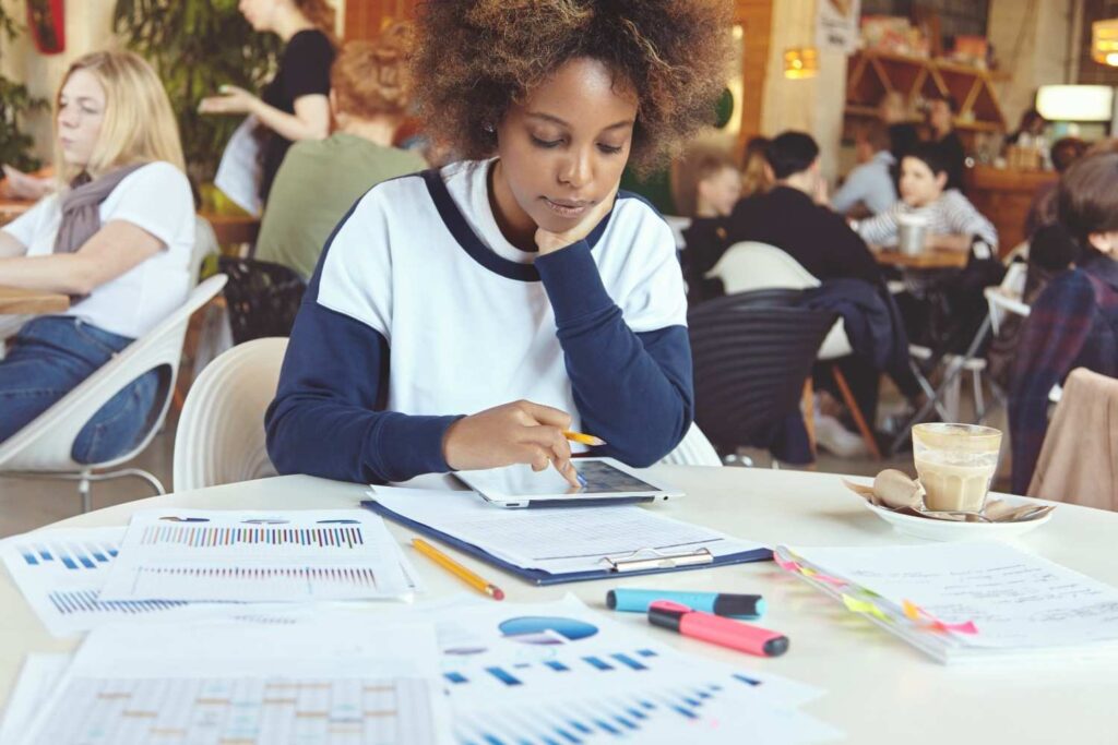 Young Nigerian writing investment plans in journal with financial resources nearby